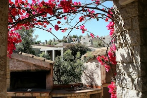 A stone building with a traditional tiled roof, surrounded by lush greenery and pink flowers. - Le Residenze di Sant'Elmo (Castiadas)