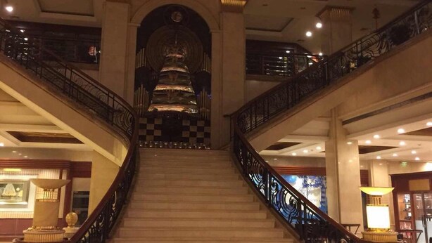 A grand staircase with ornate railings, a red lantern, and a chandelier, leading to a high-ceilinged area with a checkered floor pattern. - Inn Fine Hotel (Dalian)