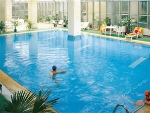 An indoor swimming pool with clear water, surrounded by lounge chairs and potted plants.