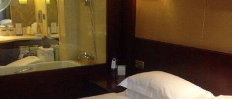 Habitación de hotel con cama, un espejo grande, ducha y una lámpara de pared.