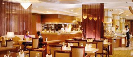 Un comedor de hotel con varias mesas y sillas, una zona de bar central y una cocina al fondo.