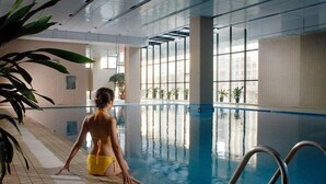 An indoor swimming pool with clear glass walls, tiled floor, and metal pool ladders. - Inn Fine Hotel (Dalian)