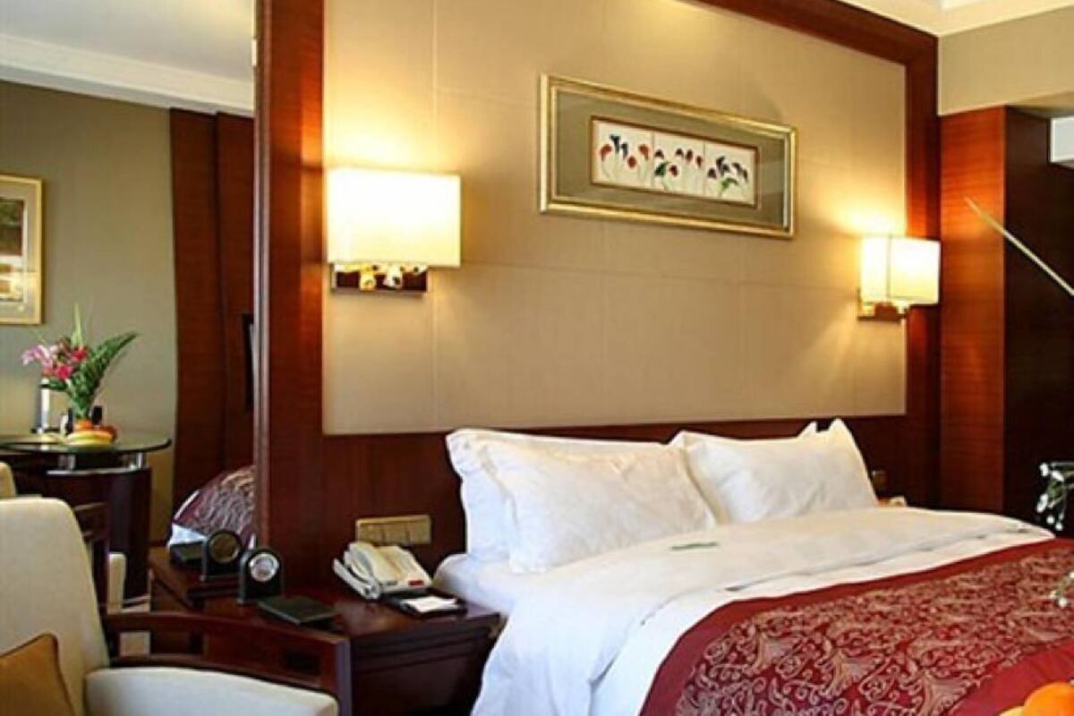 A hotel room with a large bed, two bedside lamps, a framed artwork on the wall, a nightstand with a telephone, and a small table with a vase of flowers.