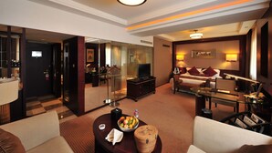 A hotel room with a living area, a television, a glass coffee table with fruit, a sofa, and a dining table. - Inn Fine Hotel (Dalian)