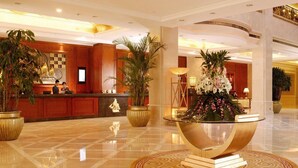 A hotel lobby with a reception desk, large potted plants, a central decorative table, and a polished marble floor. - Inn Fine Hotel (Dalian)