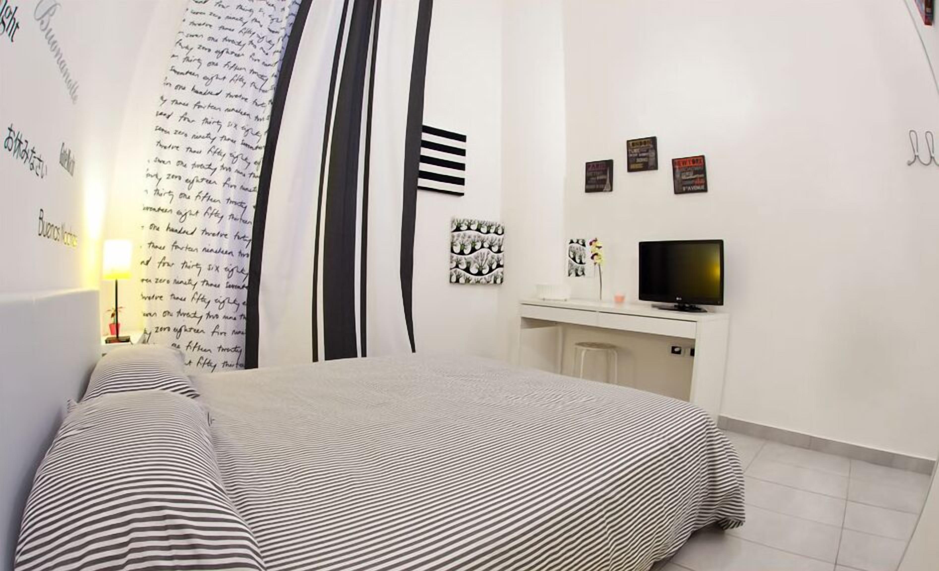 Une chambre à coucher avec un lit, un bureau, une télévision et un mur orné de textes et d’images.