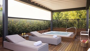 Un espace de détente extérieur abrité, comprenant deux chaises longues, un jacuzzi et une petite table avec des bougies.