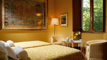 Une chambre d’hôtel avec deux lits, une carte accrochée au mur, une lampe, un tableau encadré et une fenêtre donnant sur des arbres.