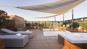 Une terrasse en bois avec des chaises longues, un jacuzzi et un espace ombragé.