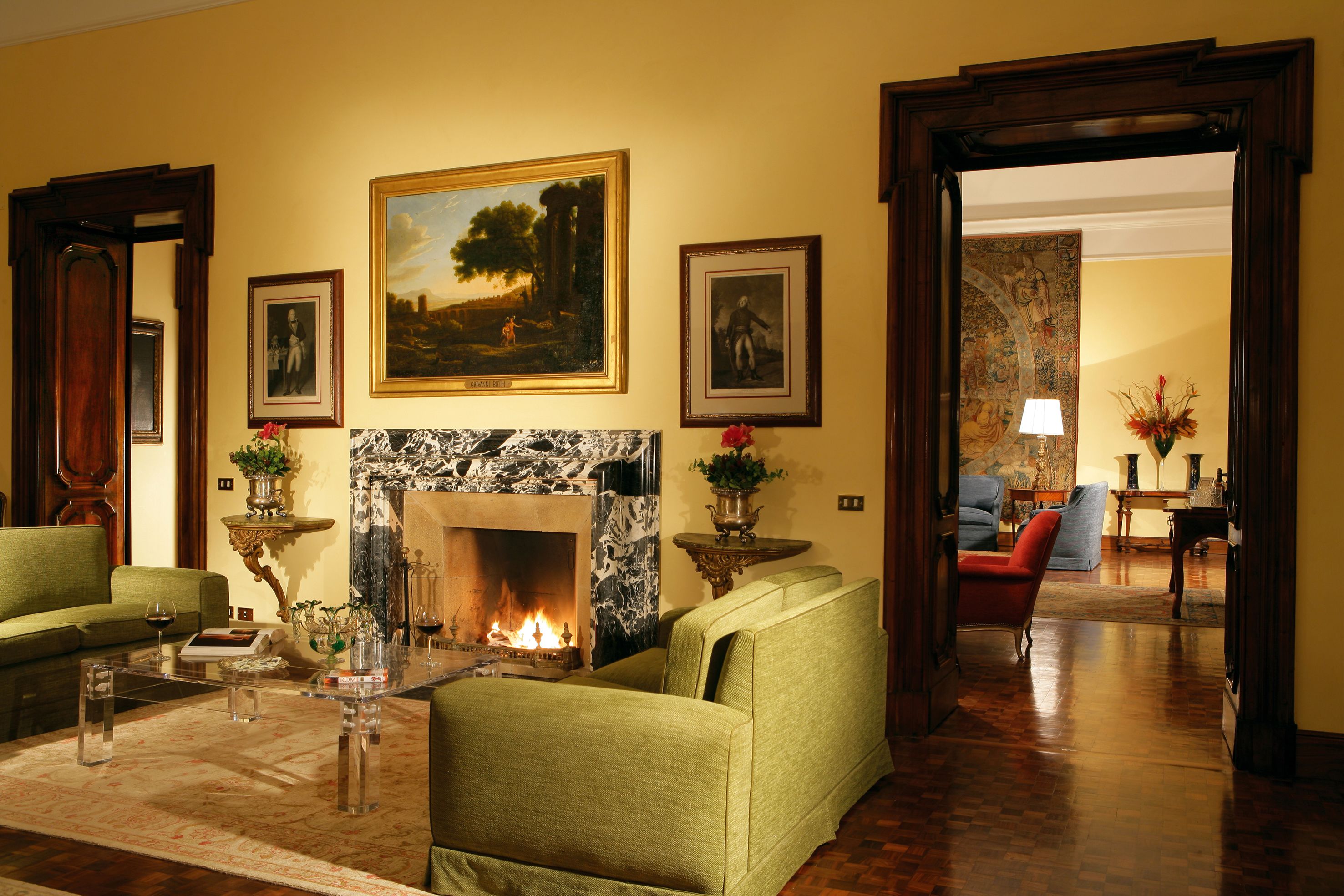 Een stijlvol ingerichte woonkamer met een open haard, groene fauteuils en een eethoek met een tafel en stoelen.