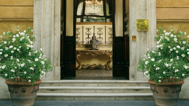 Une entrée imposante, ornée de colonnes décoratives, un balcon élégant et une grande plante en pot.