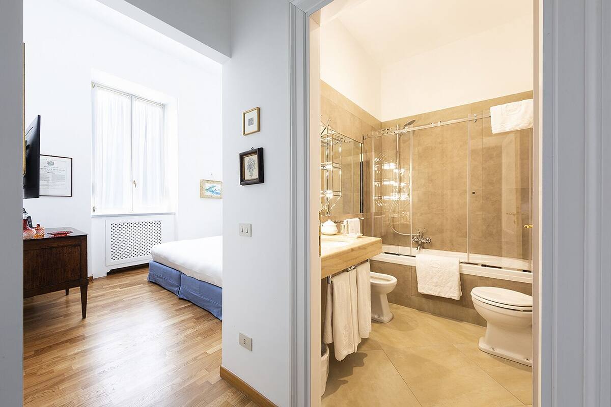 Una camera da letto con un letto, una cassettiera e una finestra. Nell'immagine si vede anche un bagno con doccia, un water e un lavandino.