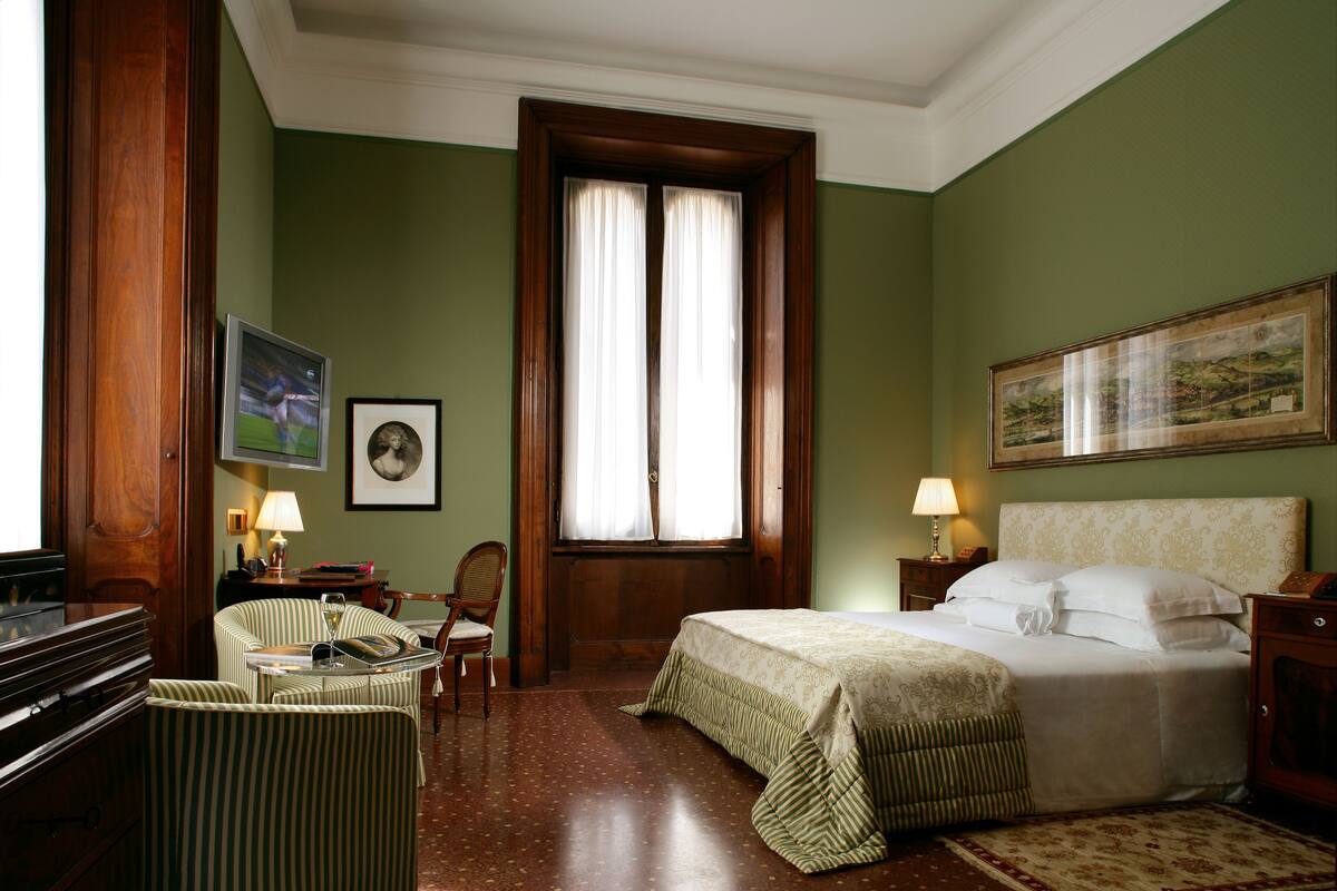 Una camera d'albergo con un letto, una sedia, una scrivania e una finestra con tende.