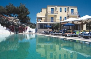A pool area with lounge chairs and umbrellas, a building with balconies, and a tree with flowers. - Hotel San Vito (Forio)