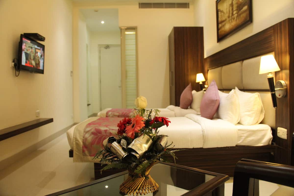 Une chambre d’hôtel avec un lit, des lampes de chevet, un téléviseur fixé au mur et un vase avec des fleurs sur la table.
