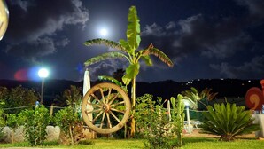 Escena nocturna con una gran rueda de madera, una planta de plátano y una cerca en un jardín.