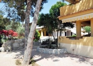 A courtyard with a yellow building, stone walls, and trees. - Residence Hotel Riviera Calabra (Zambrone)