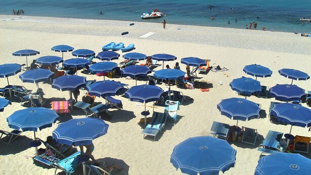 Una playa con numerosos sombrillas y sillas de playa azules.