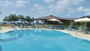 Una piscina con sillas de descanso y sombrillas, rodeada por un edificio con techo.