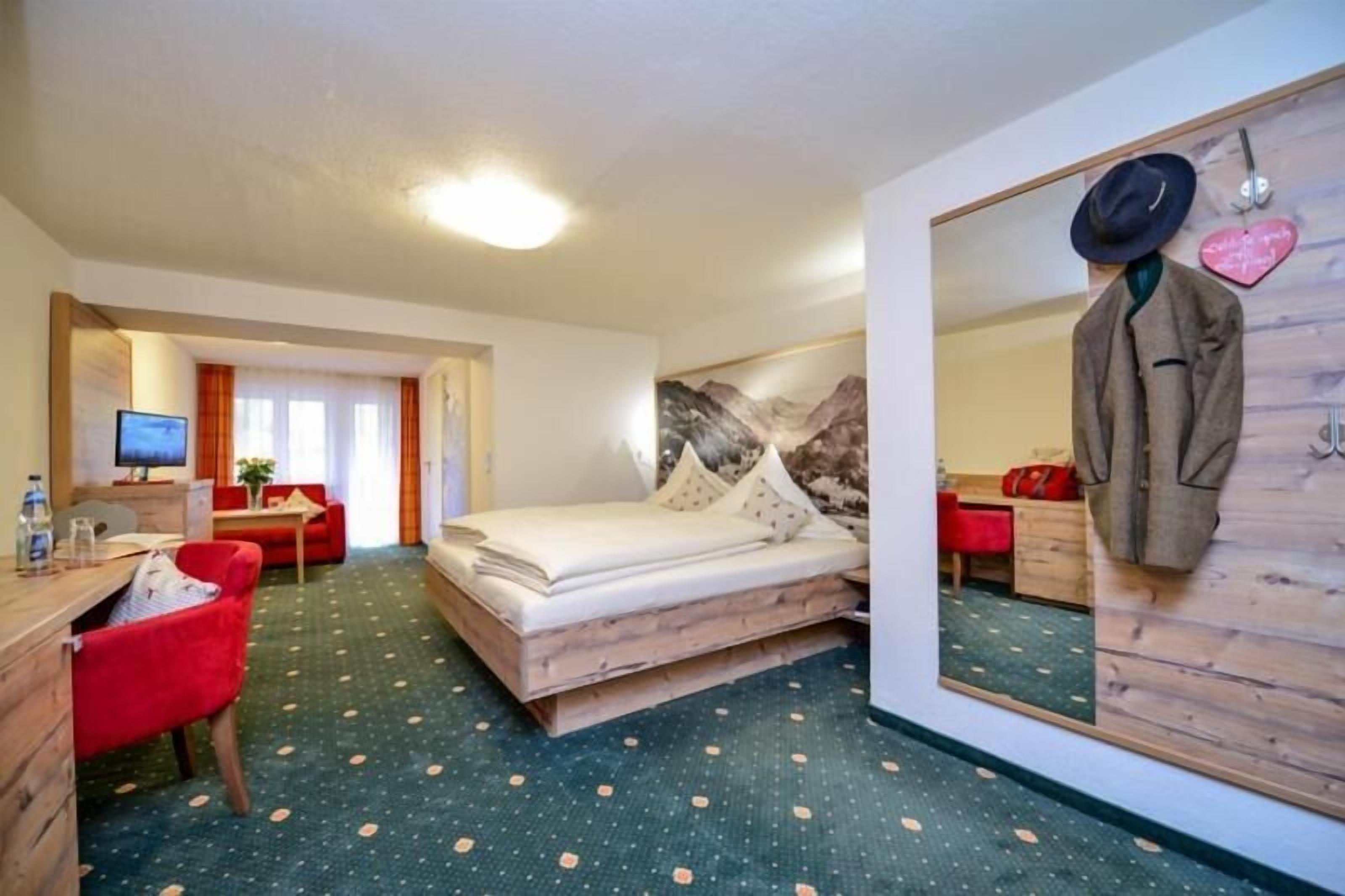Una habitación de hotel con una cama, un escritorio, una silla, un espejo y un perchero.