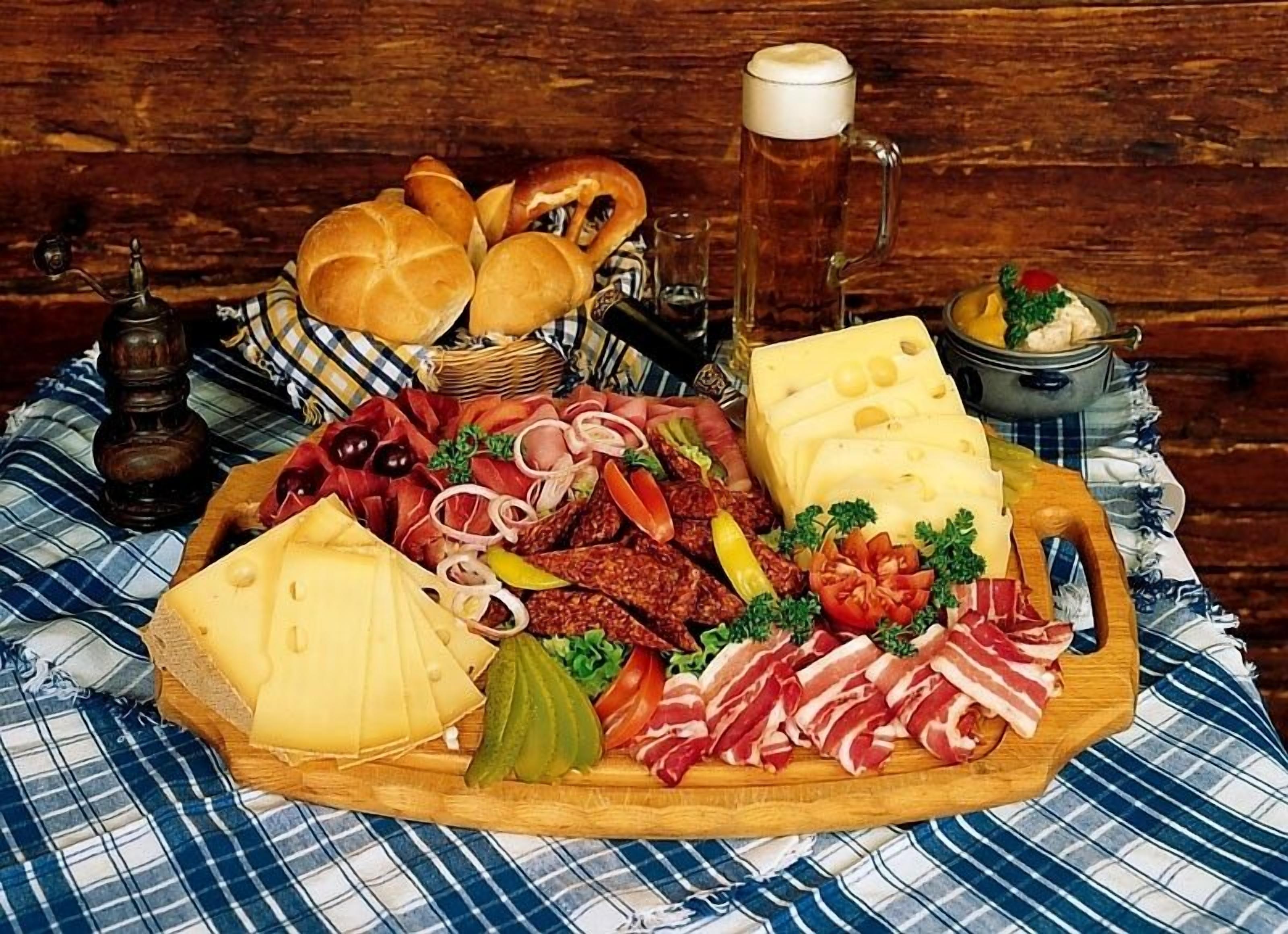 Een charcuterieplank met diverse vleessoorten, kazen en ingelegde groenten, vergezeld van brood, een bierkan en een pepermolen.