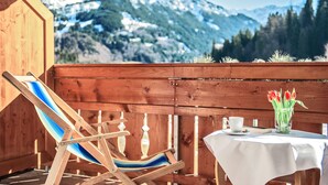 A wooden deck with a blue-striped lounge chair, a table with a white tablecloth, a cup, and a vase with red tulips. - Sonnenbichl Hotel am Rotfischbach (Fischen im Allgaeu)