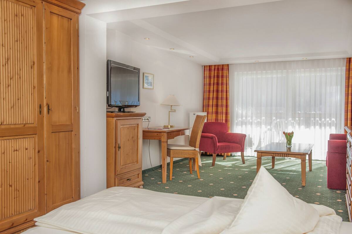 Une chambre d’hôtel comprenant un lit, un bureau avec un ordinateur, une télévision, une chaise, une table avec un vase et une armoire.