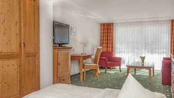 Ein Hotelzimmer mit einem Bett, einem Schreibtisch mit Computer, einem Fernseher, einem Sessel, einem Tisch mit Vase und einem Kleiderschrank.