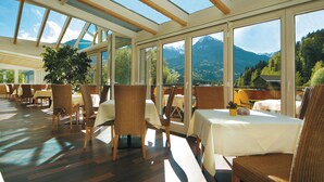 A restaurant with large windows, wooden beams, and tables set for dining. - Sonnenbichl Hotel am Rotfischbach (Fischen im Allgaeu)