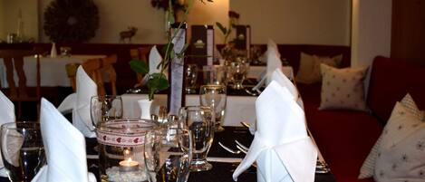 Une table à manger dressée avec des serviettes blanches, des couverts en argent et de la verrerie, agrémentée d’une bougie et d’un bouquet de roses en guise de centre de table.