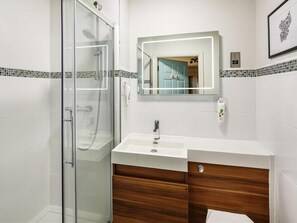 Une salle de bain avec une douche à parois de verre, un lavabo blanc avec un miroir au-dessus et un meuble-lavabo en bois.