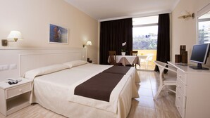 A hotel room with a large bed, bedside tables, a desk with a computer, and a balcony with a table and chairs. - Hotel Elegance Palmeras Playa (Puerto de la Cruz)