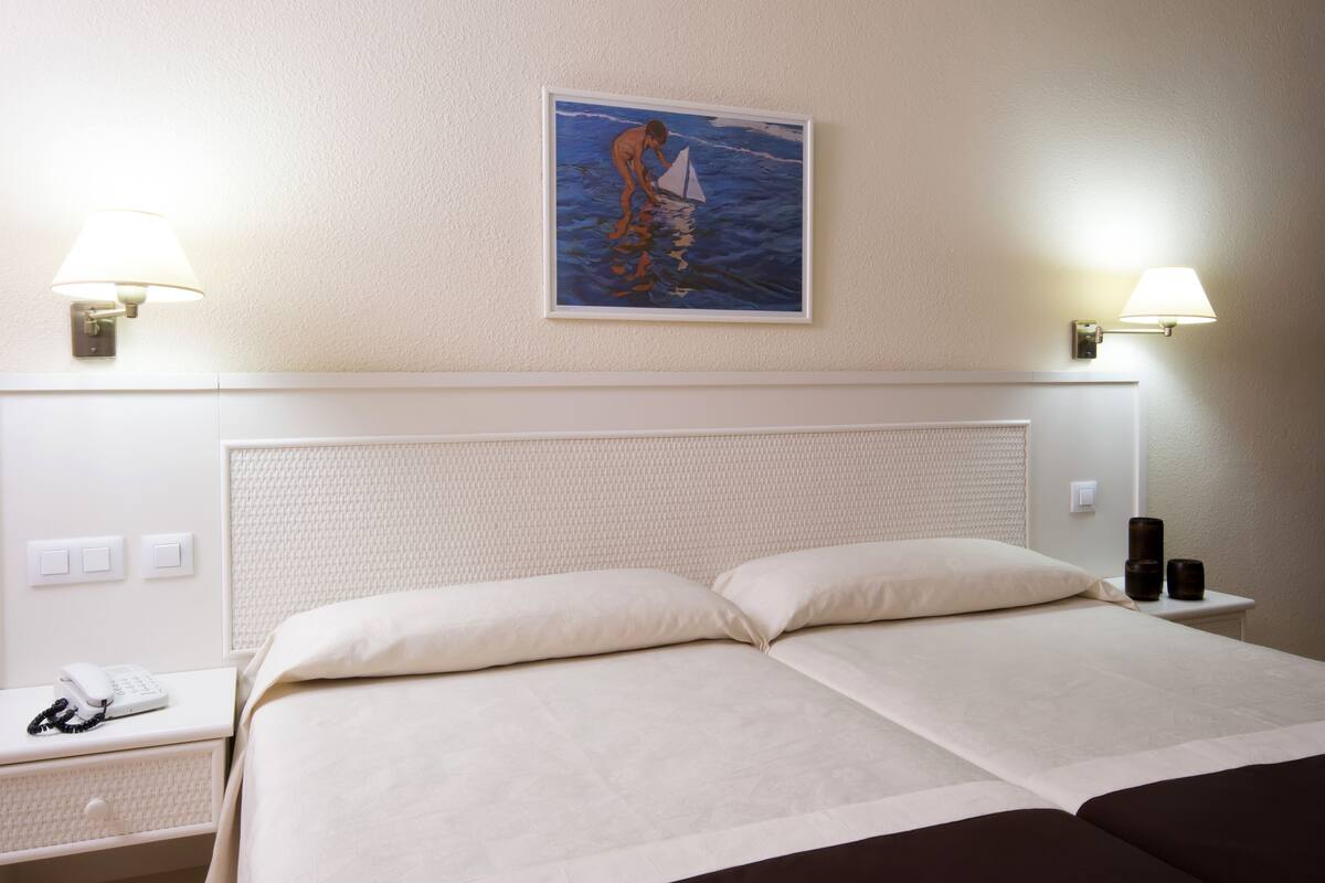 A hotel room with a bed, two bedside tables, a lamp, and a painting on the wall.