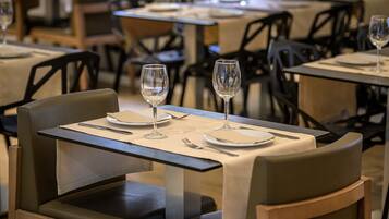 Comedor con mesas dispuestas para dos, cada una con una copa de vino, cubiertos y servilleta.