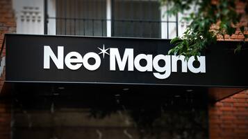 Un letrero con el texto 'Neo*Magna' sobre un fondo negro.