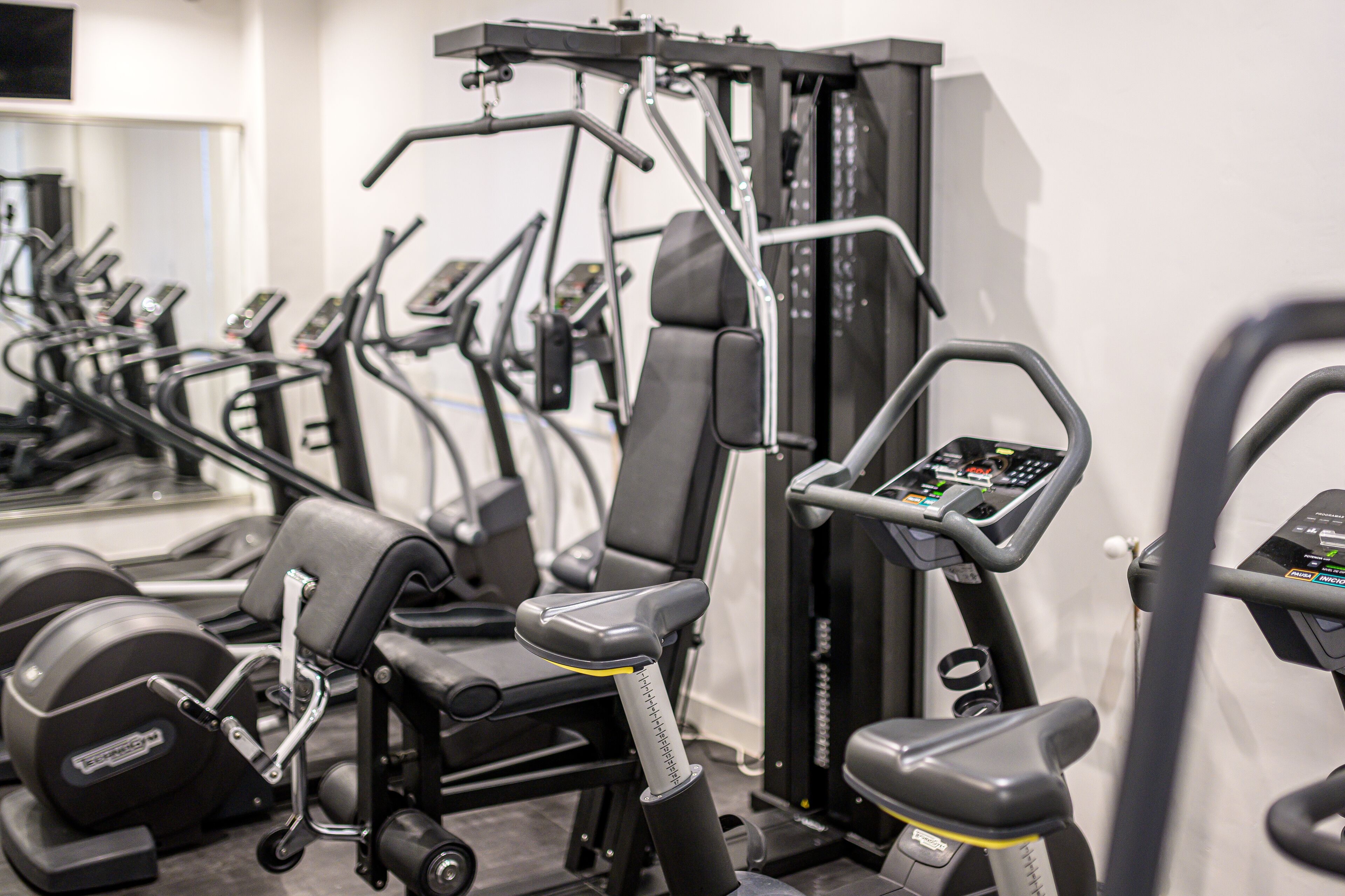 Een sportschool met diverse fitnessapparaten, waaronder loopbanden, een krachttrainingapparaat en gewichten.