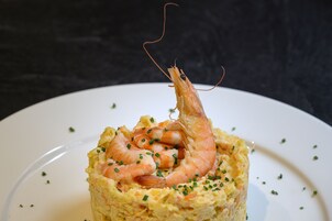 Un piatto con gamberi su un letto di riso, guarnito con erbe aromatiche.