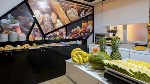 Un bufé con diversas opciones de comida, incluyendo frutas, pasteles y pan.