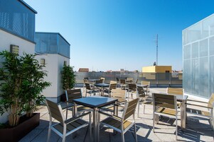 Un'area esterna con tavoli e sedie, circondata da piante in vaso, con vista sulla città.