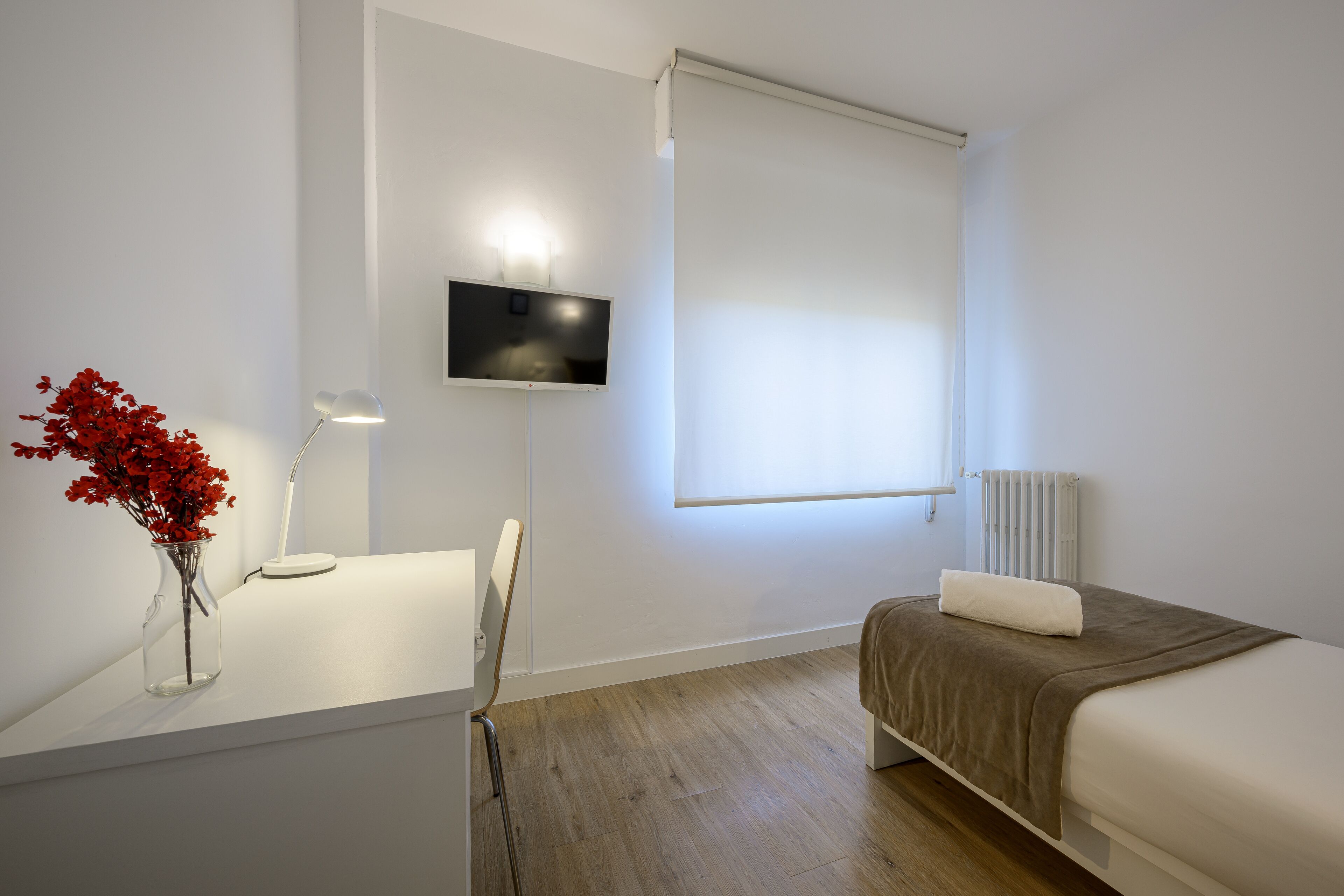 Ein Hotelzimmer mit einem Bett, einem Schreibtisch mit Lampe, einem Fernseher und einem Fenster mit Jalousie.