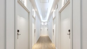 Un pasillo largo y estrecho con paredes blancas y suelo de madera, que conduce a varias puertas numeradas.