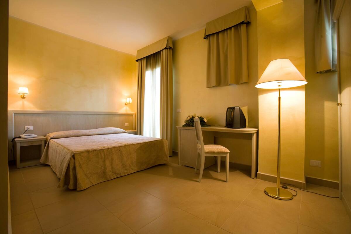 Une chambre d’hôtel équipée d’un lit, d’un bureau, d’une chaise, d’une lampe et de rideaux.