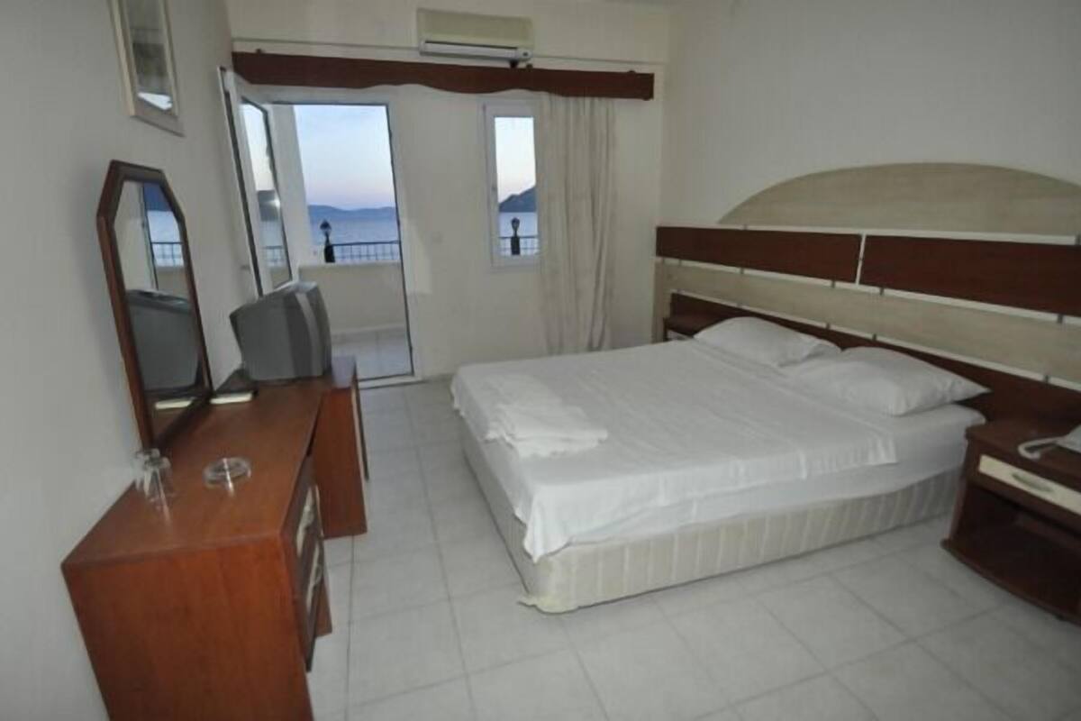 Quarto de hotel com cama, cómoda de madeira, espelho e janela com vista.