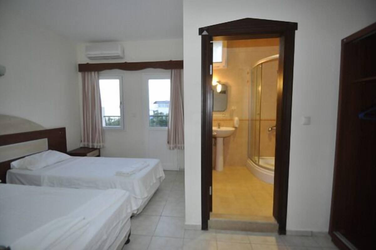 Quarto de hotel com duas camas, banheiro com chuveiro e vista para o exterior.