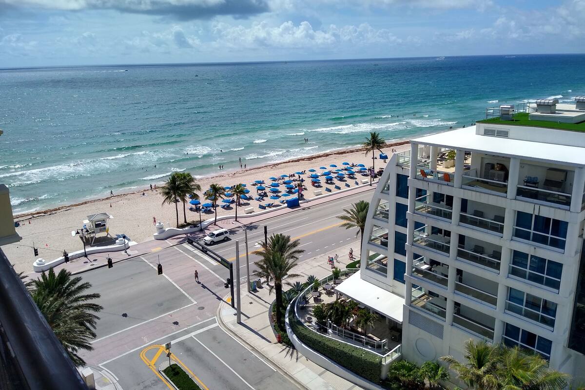 A beachside view with a road leading to a building with multiple floors and balconies.