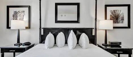 Quarto de hotel com uma cama grande, duas mesas de cabeceira, uma cabeceira e obras de arte emolduradas nas paredes.