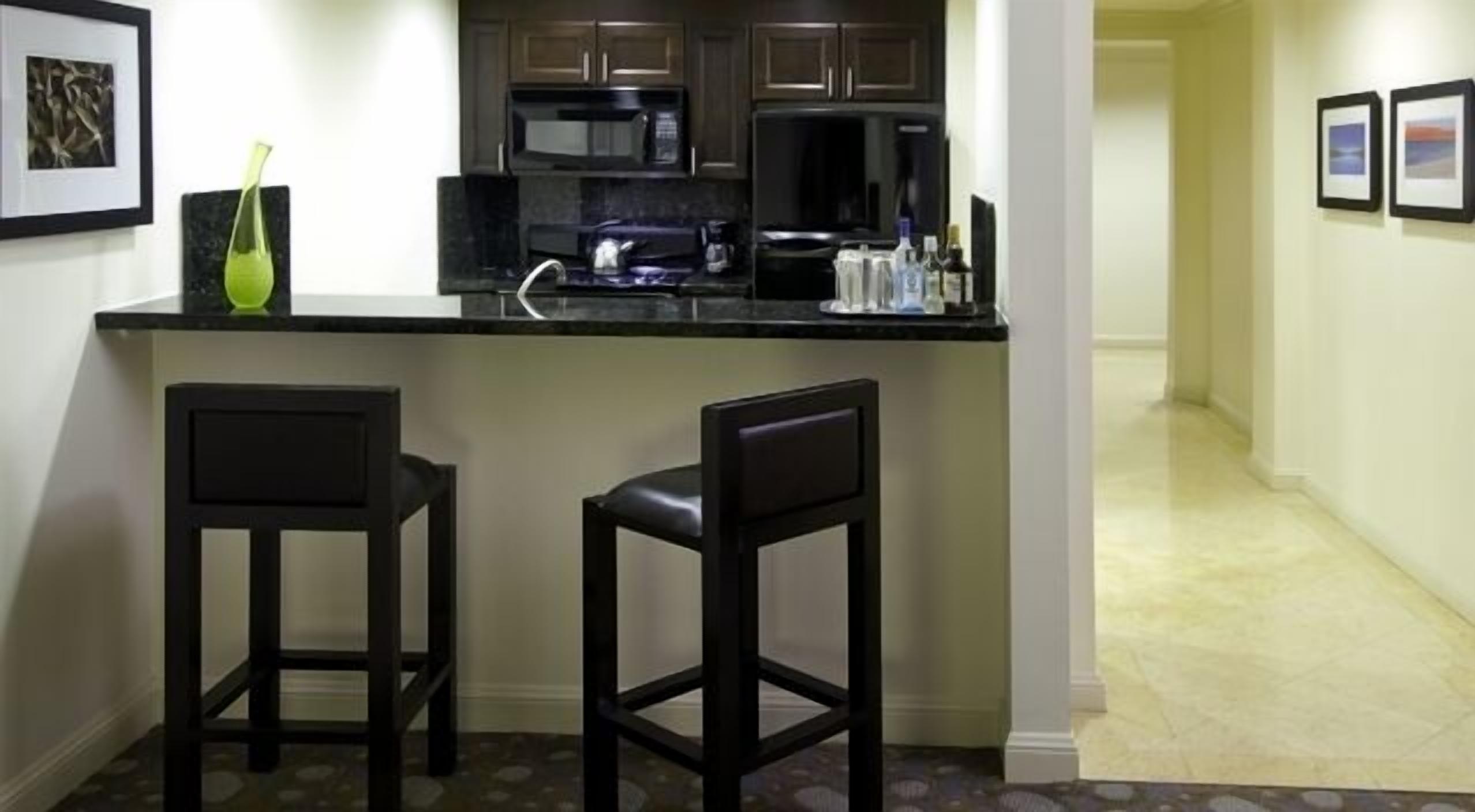 A small kitchen area with a black countertop, two bar stools, a microwave, and a coffee maker.