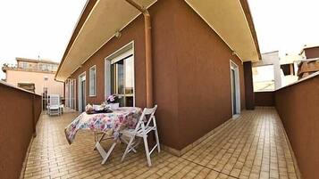 A covered outdoor area with a table and chairs, a tiled floor, and a building with a brown exterior.