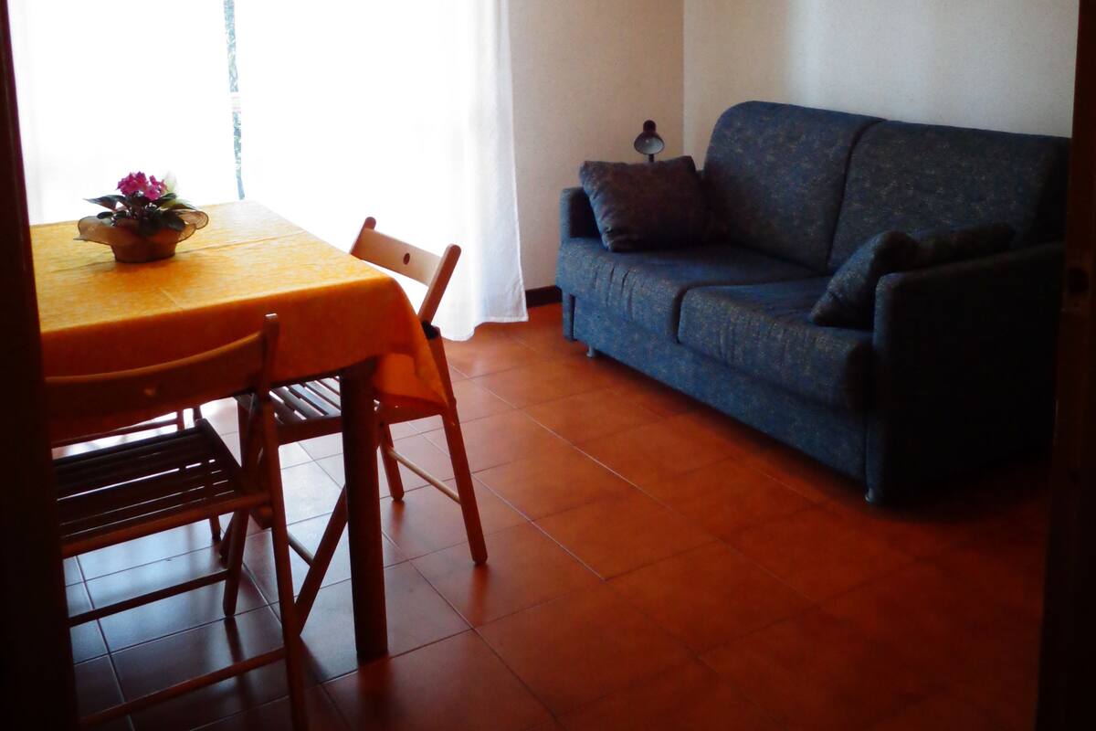 Uma área de refeições com uma mesa e cadeiras, um sofá e uma janela com cortinas.
