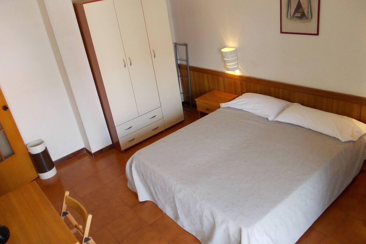 Quarto com cama, guarda-roupa, mesa de cabeceira, luminária na parede e quadro emoldurado.